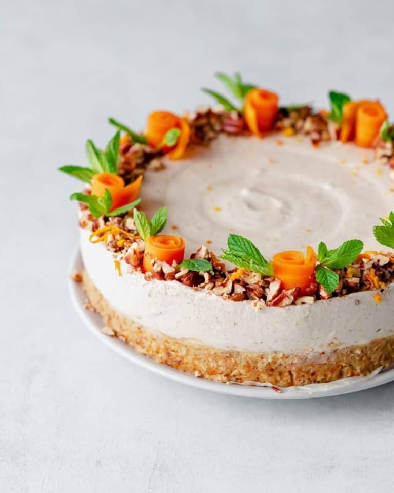 A vegan cheesecake topped with scrolls of carrot and herbs around the edge.