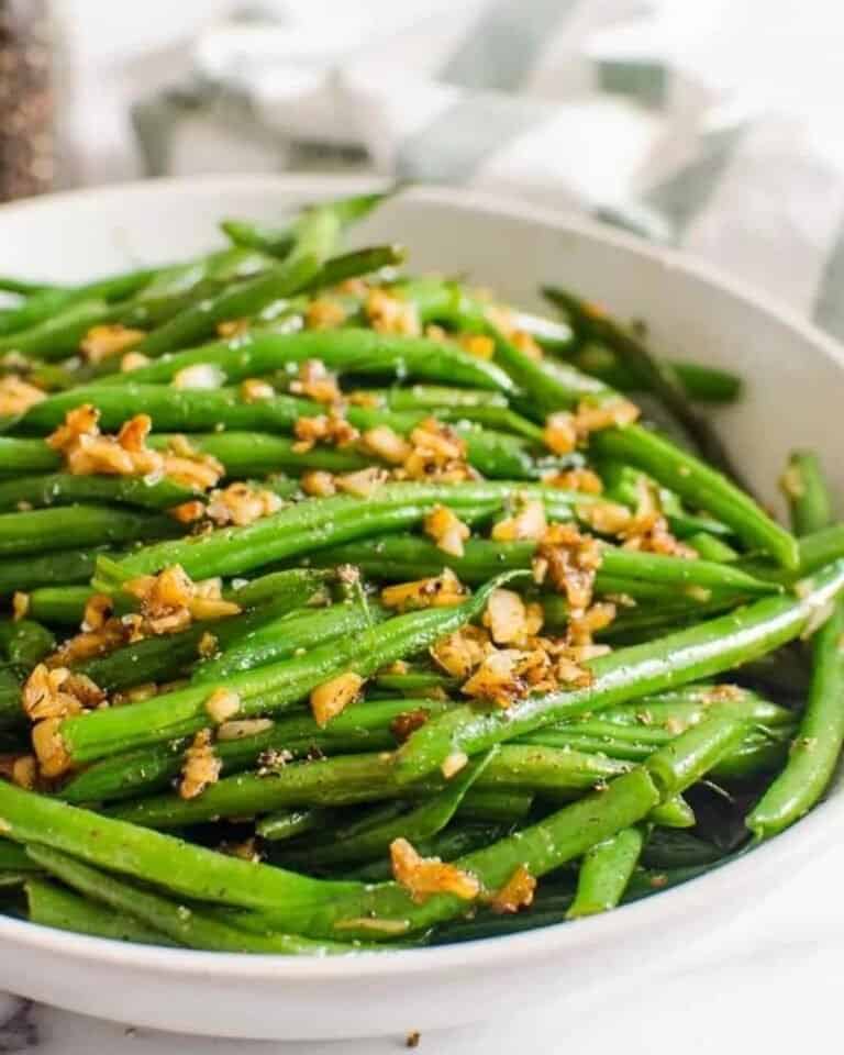 Cooked green beans in a dish topped with fried garlic.