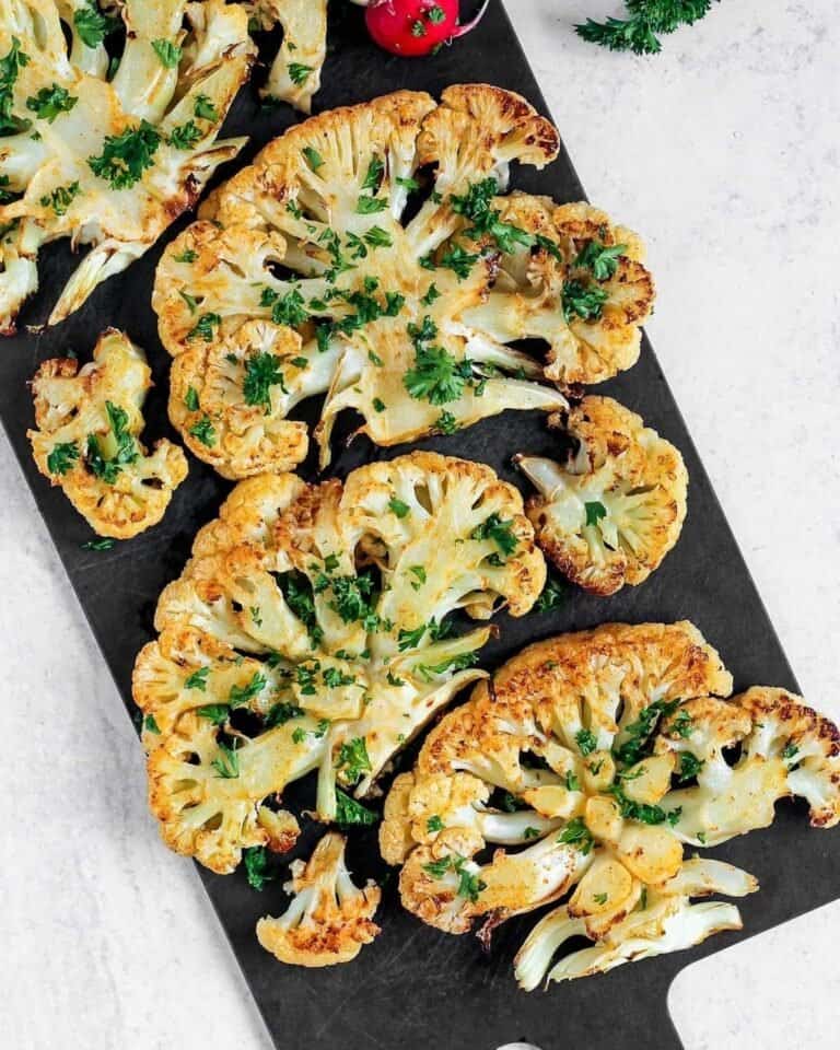 Cauliflower steaks on a board topped with herbs.