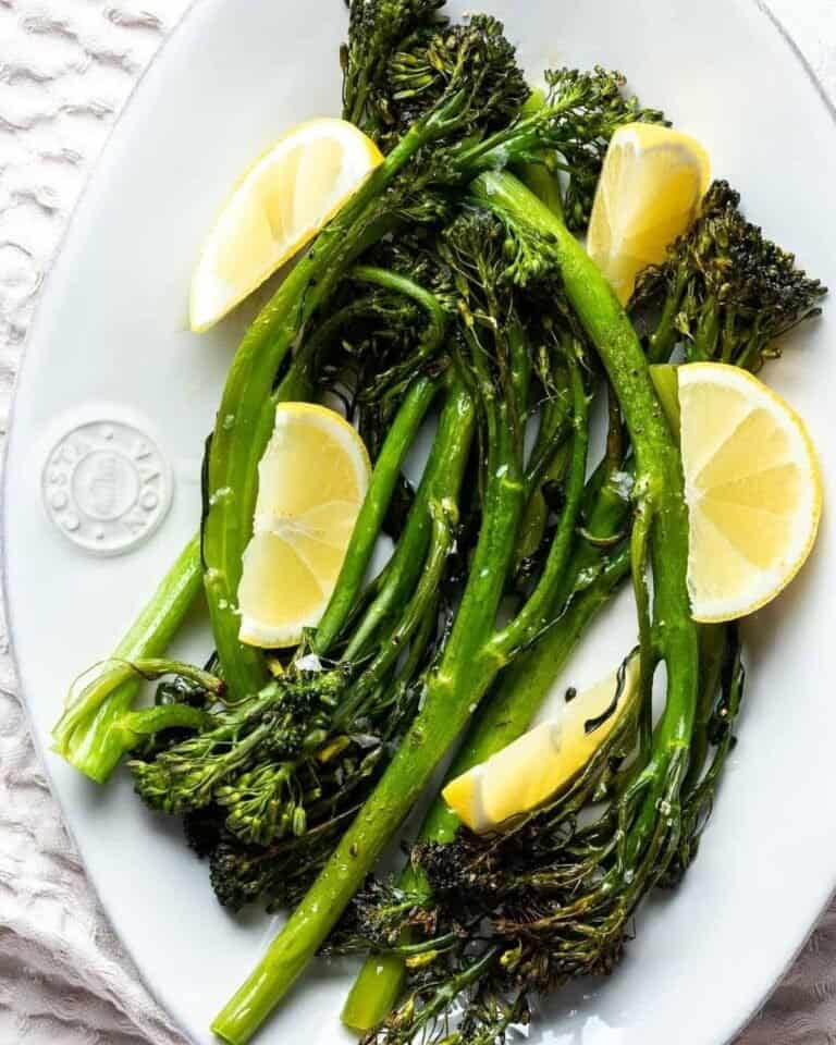 Roasted tenderstem broccoli on a serving plate with slices of lemon.