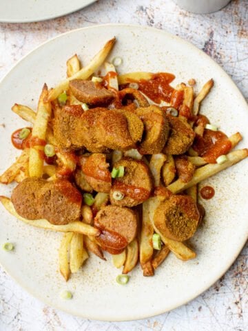 Overhead view of vegan currywurst served on a bed of fries topped with curry ketchup.