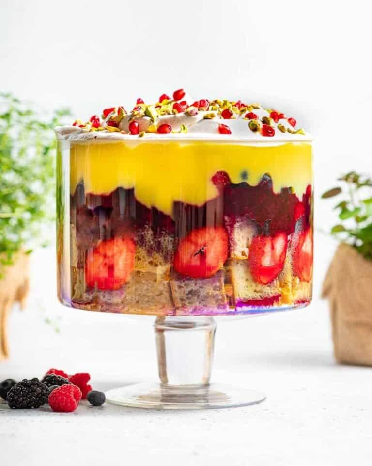 A large vegan trifle in a large glass trifle bowl with fruit on top.