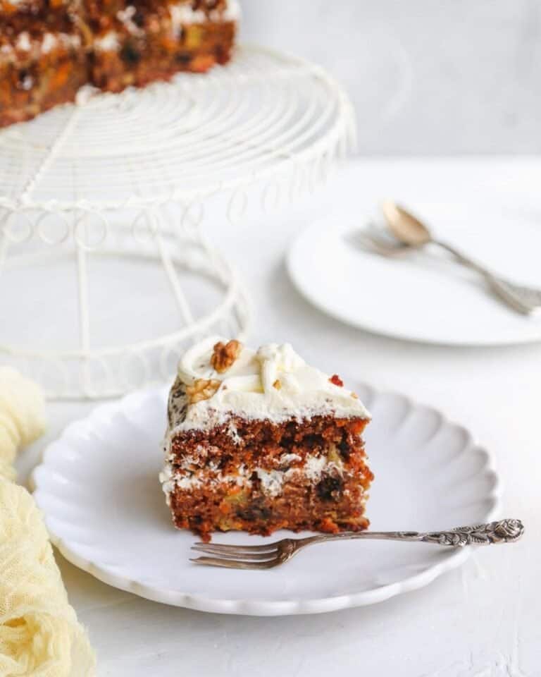 A slice of vegan carrot cake with the full cake in the background.