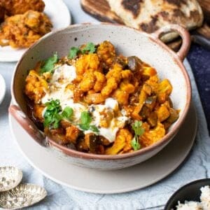 Aubergine curry with cauliflower with spoons, friend Indian snacks and Indian bread.