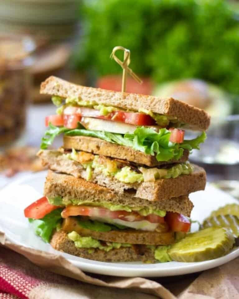 Vegan club sandwich on a plate with gherkins.