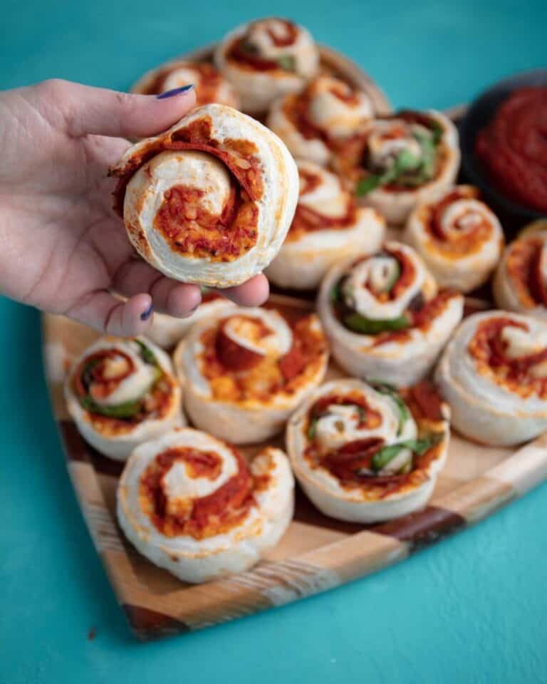A board of pizza swirls, one is held up to the camera by a hand.