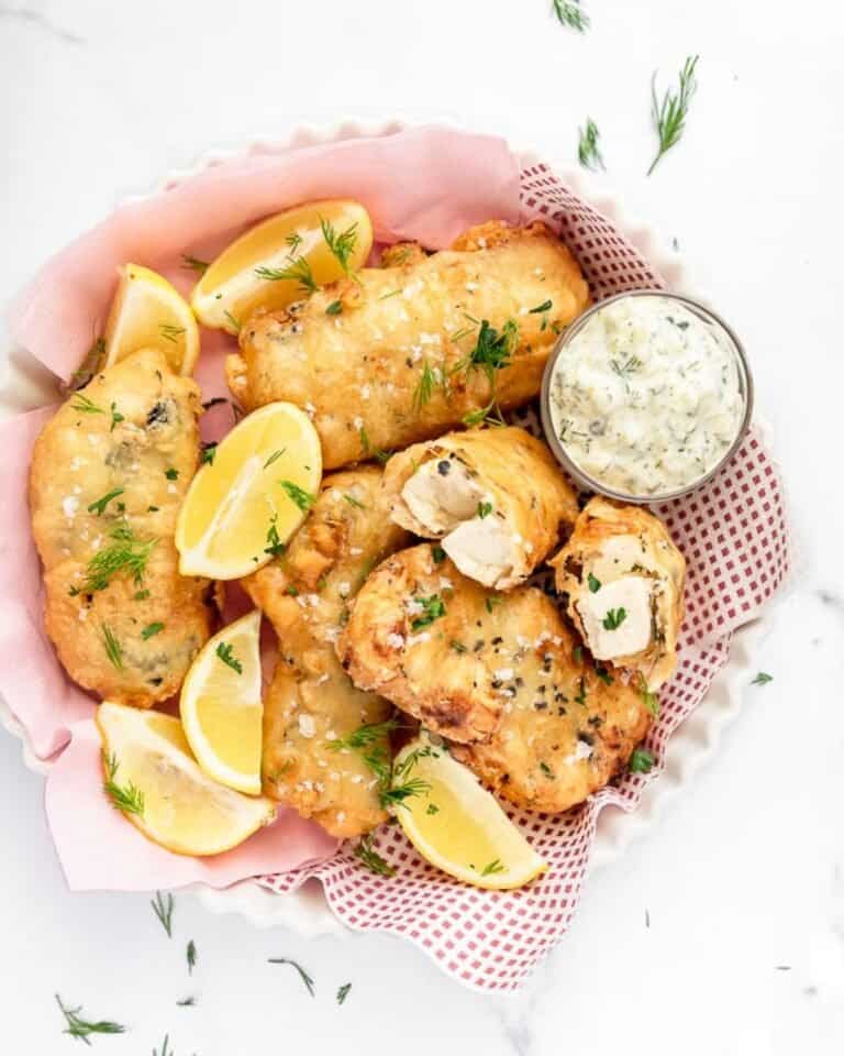 A lined basket of battered tofish served with wedges of lemon and tartare sauce.
