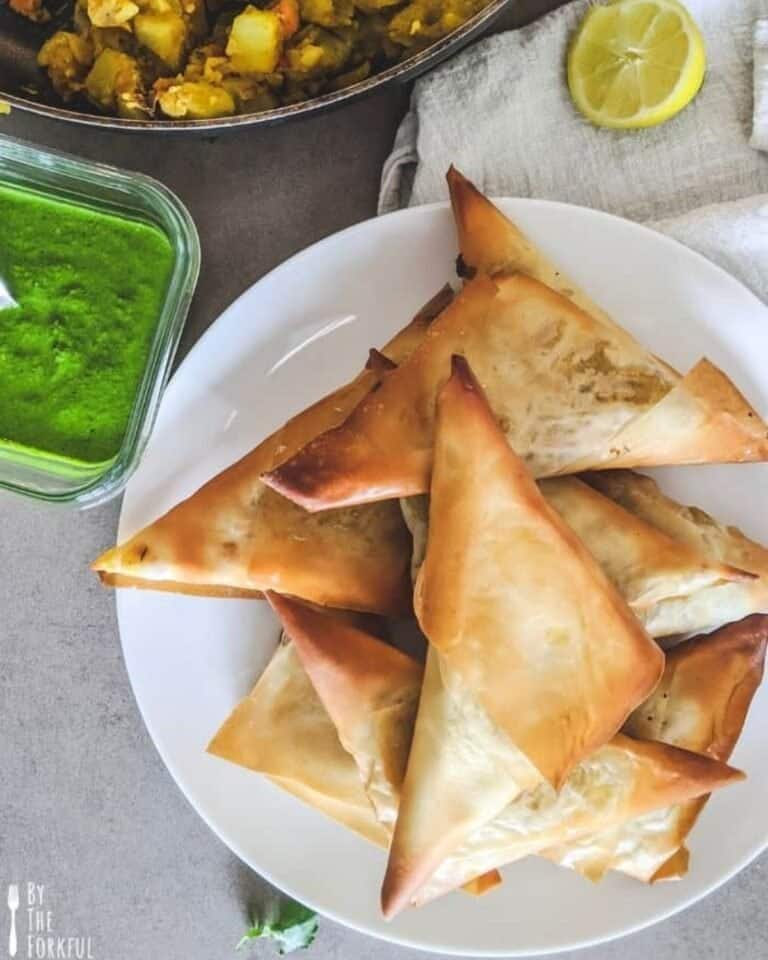 A plate of vegetable samosas piled high with coriander chutney to the side.