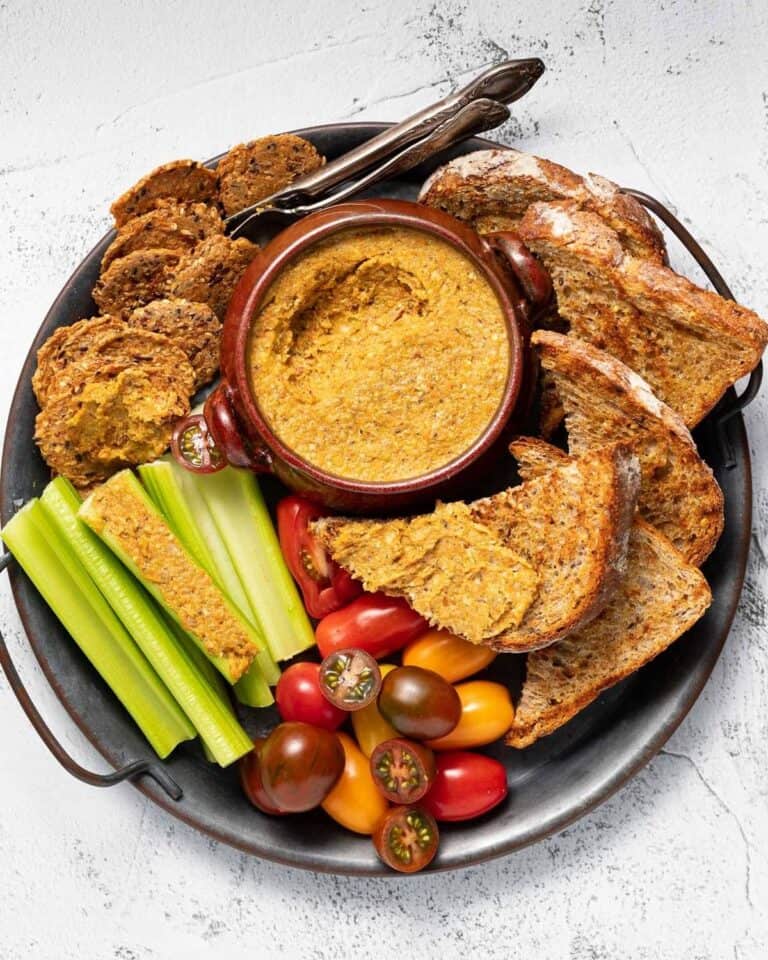 A platter of vegetable pate, toast, crackers, celery sticks and tomatoes.