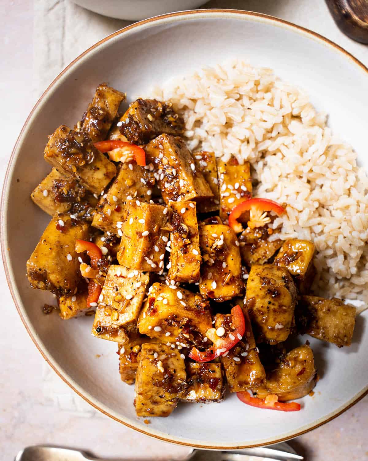 Szechuan tofu in a bowl topped with sesame seeds, served with brown rice.