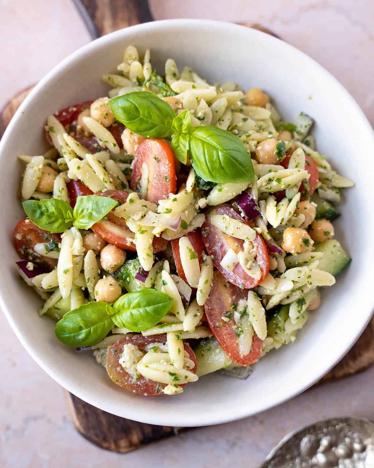 Pesto orzo salad in a white bowl with fresh basil on top.