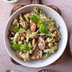 Pesto orzo salad in a bowl with chickpeas, grape tomatoes and fresh basil.