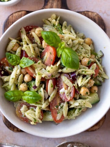 Pesto orzo salad in a bowl with chickpeas, grape tomatoes and fresh basil.