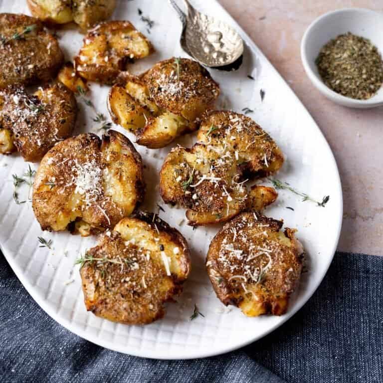 Smashed potatoes on a plate topped with fresh thyme and vegan parmesan cheese.
