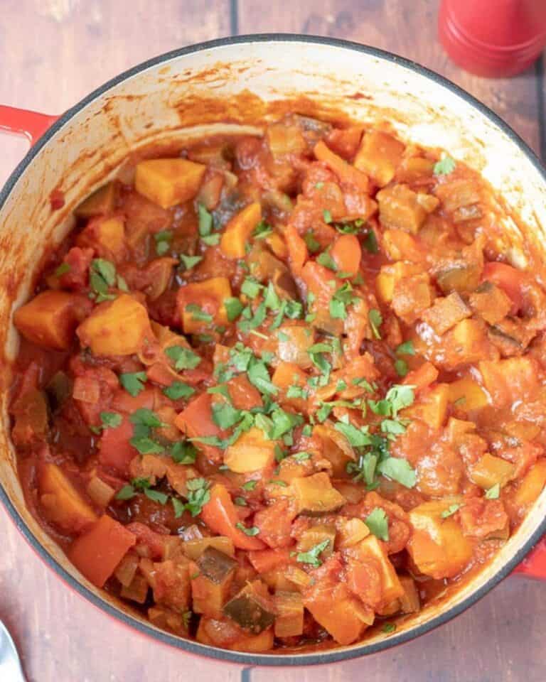 Aubergine and sweet potato curry topped with fresh coriander in a large pot.