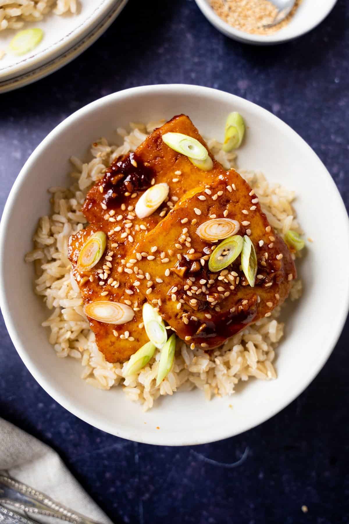 Slices of gochujang tofu with spring onions, sesame seeds and rice.