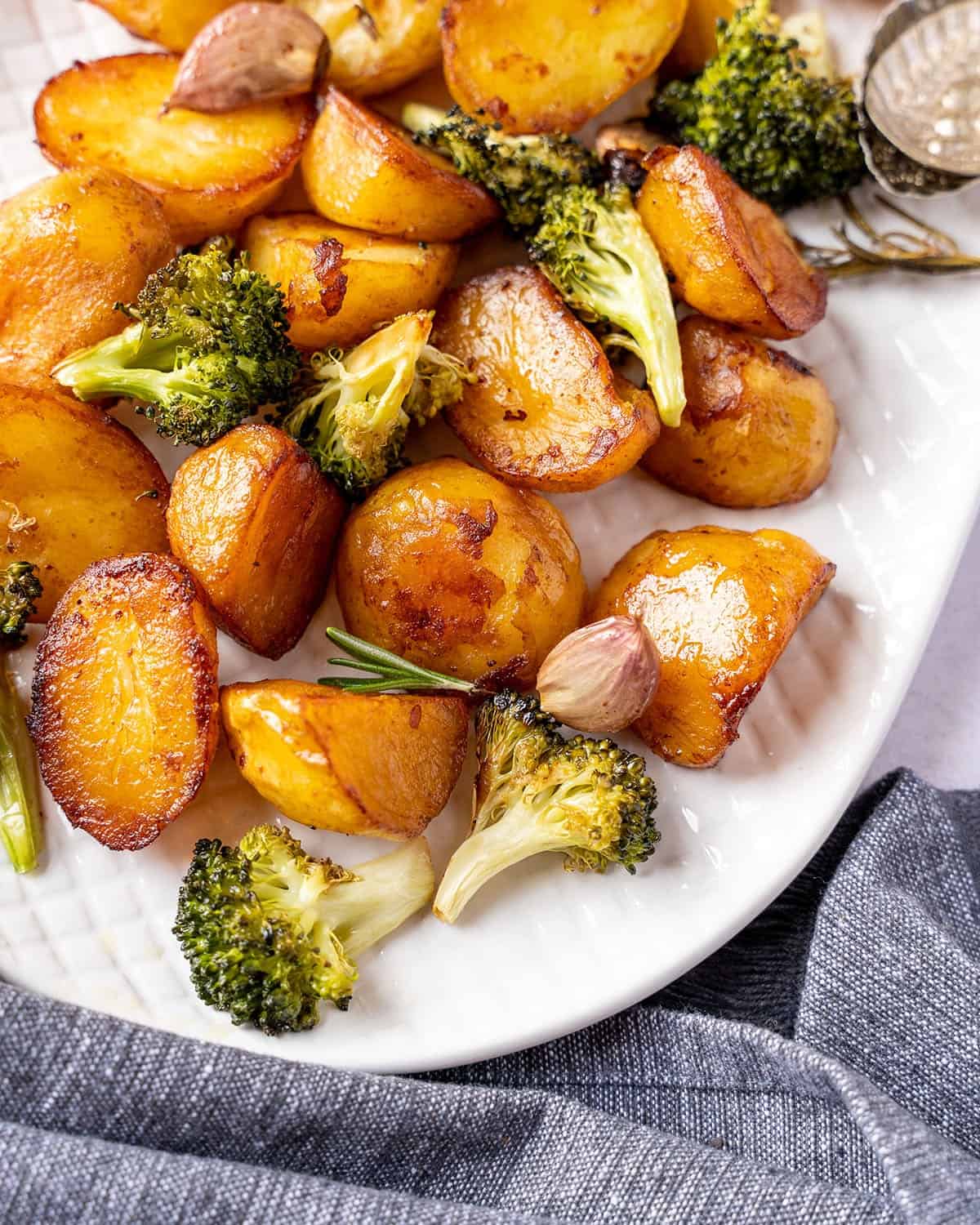 Marmite roast potatoes on a serving plate with broccoli and garlic cloves.