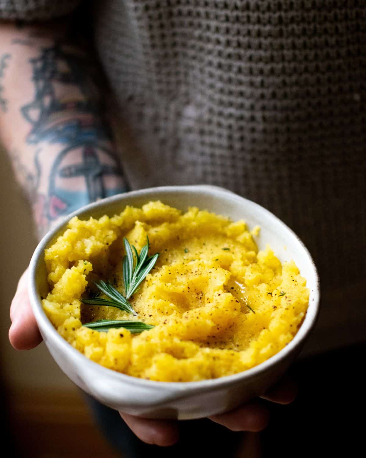 A hand holding a bowl of mashed swede.