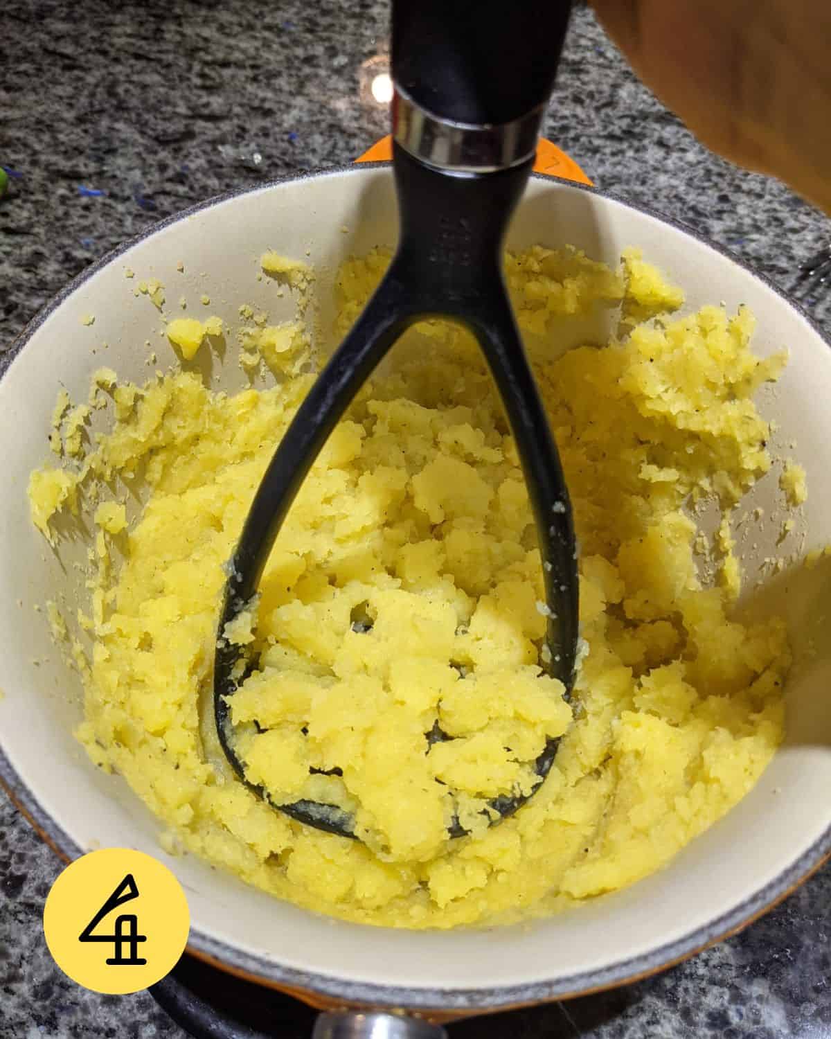 Swede being mashed with a potato masher in a pan.