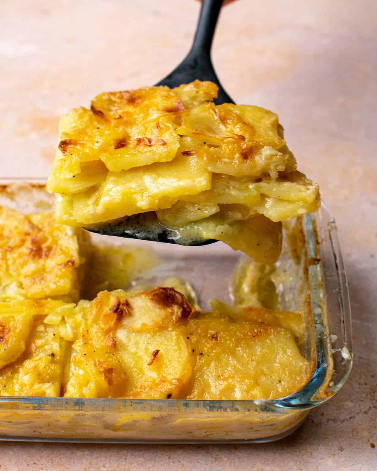 A spatula full of dauphinoise potatoes held above the cooked finished dish.