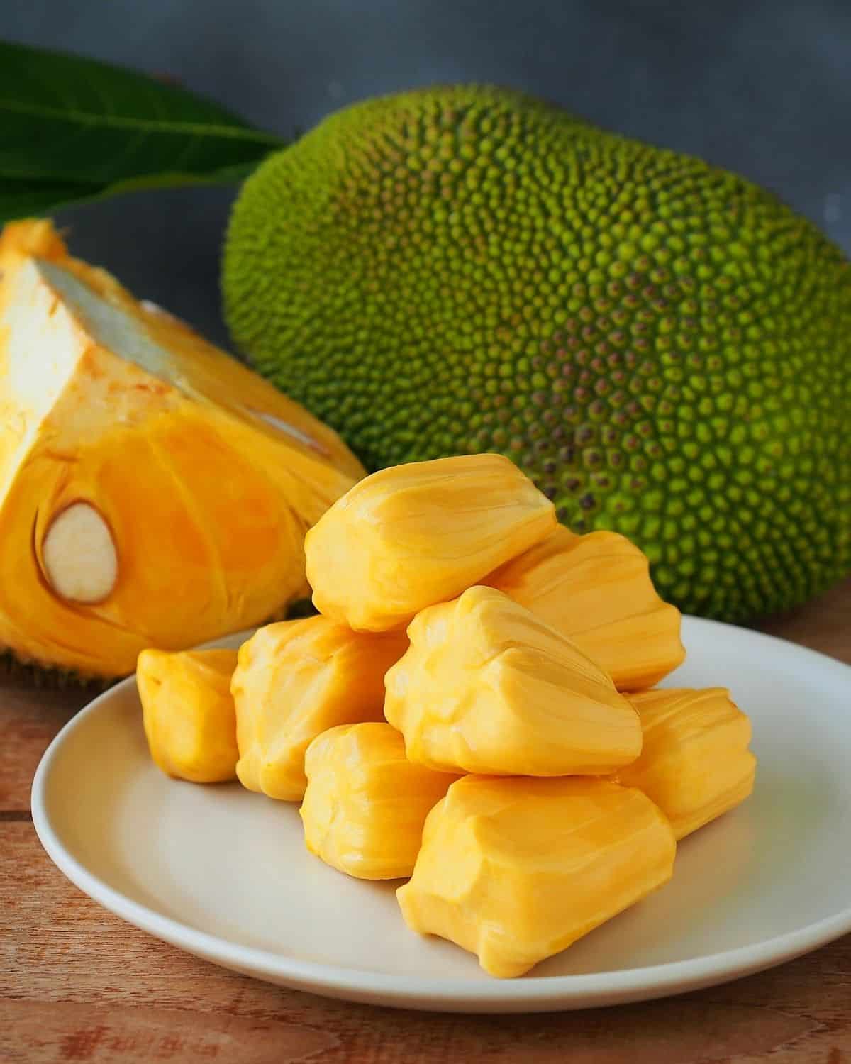 Ripe jackfruit on a plate with a whole jackfruit behind it.