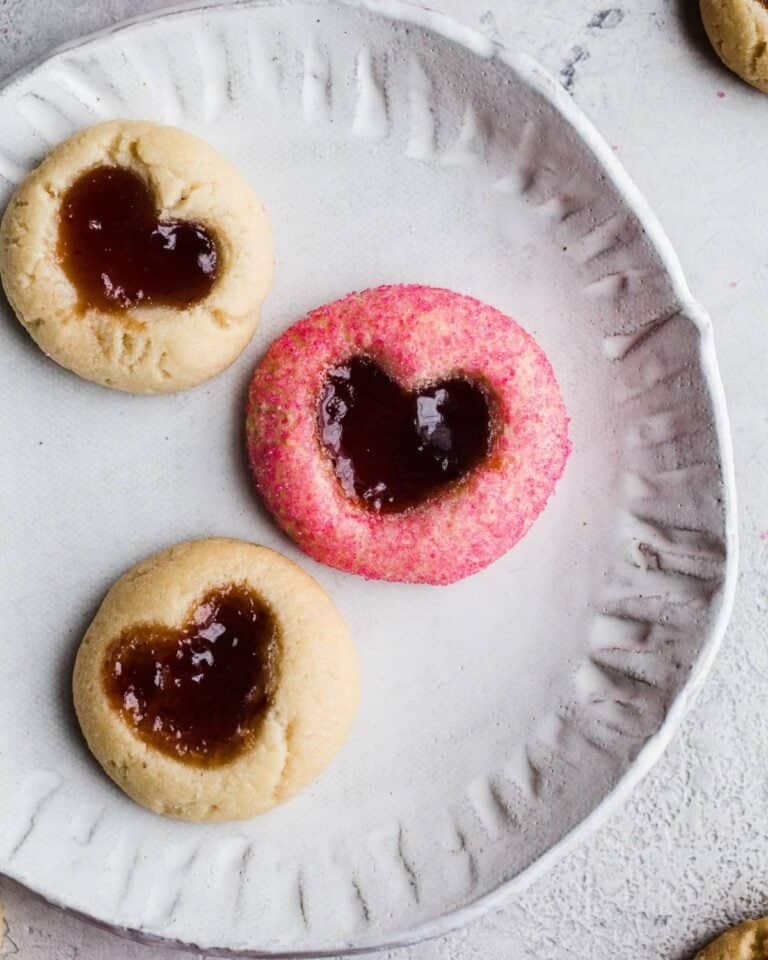Heart thumbprint biscuits with jam on a ceramic plate.