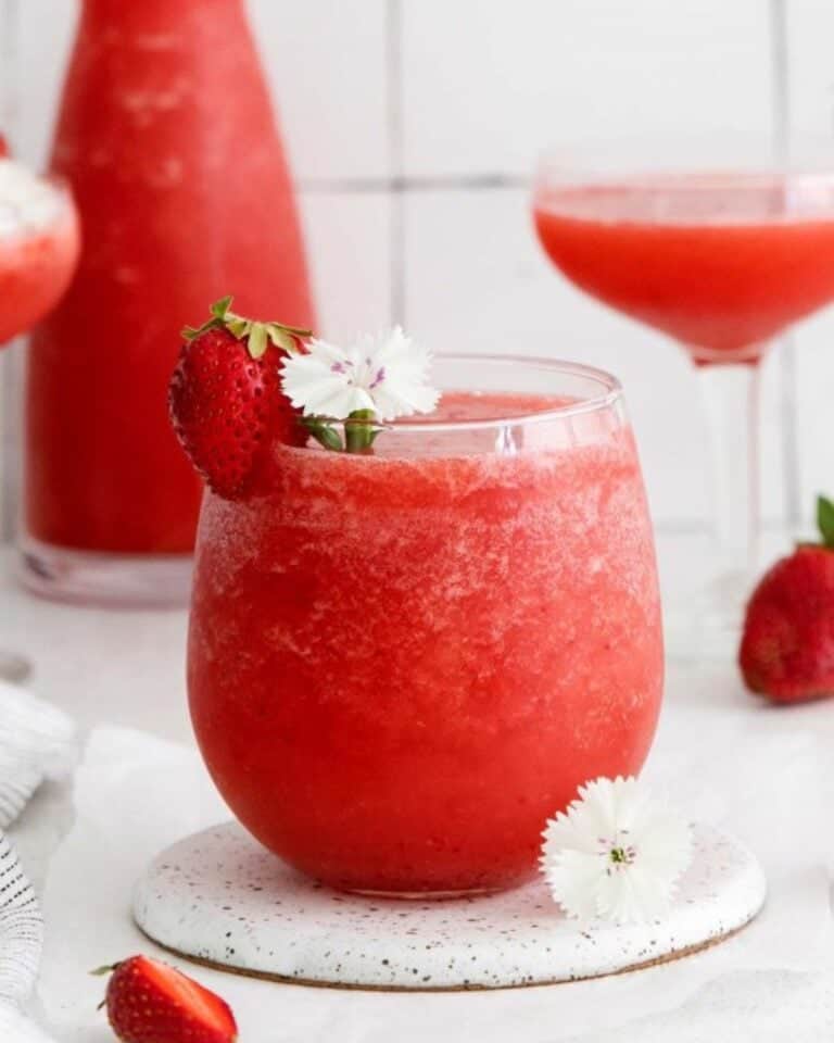 A small tumbler of strawberry frosé with a strawberry on the side of the glass.