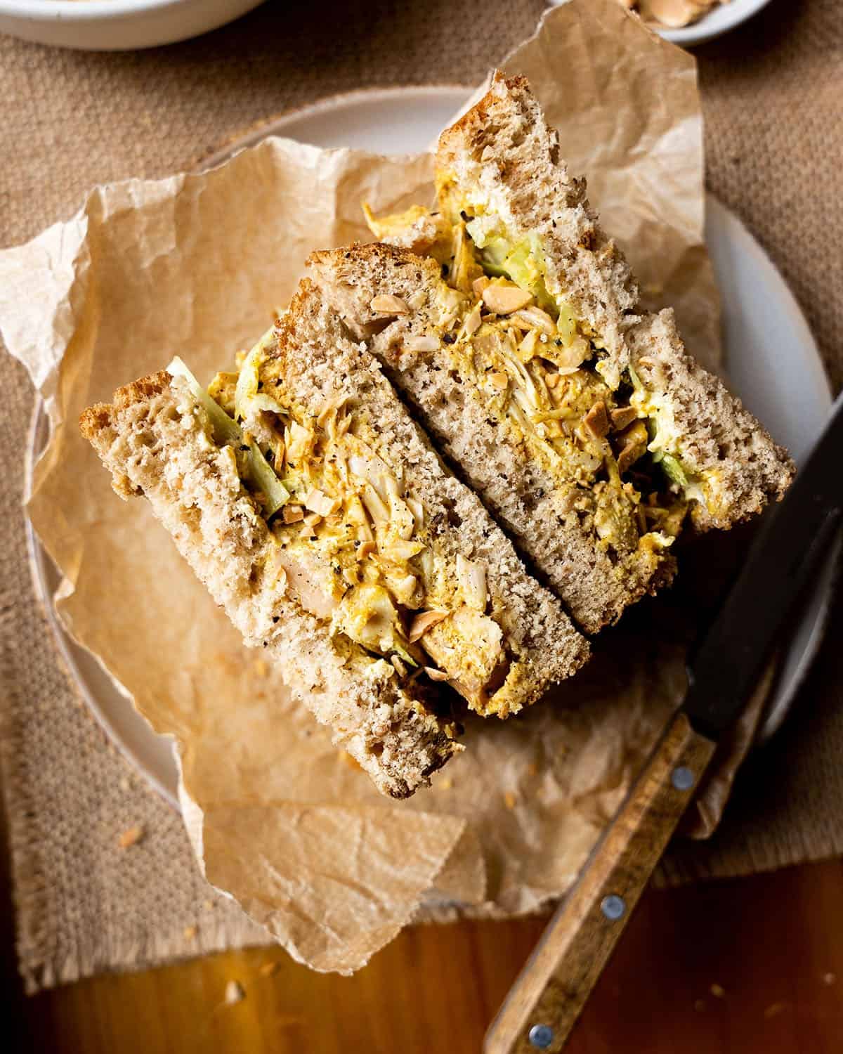 Vegan coronation chicken sandwich on a plate with a knife.