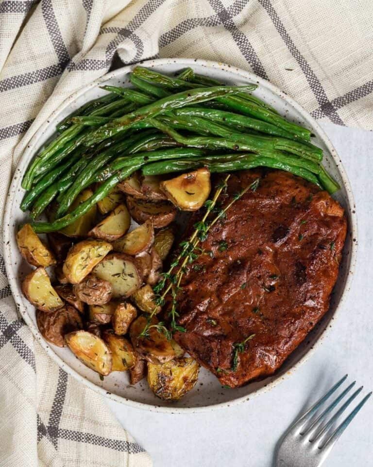 Vegan steak dinner on a plate with green beans and potatoes.