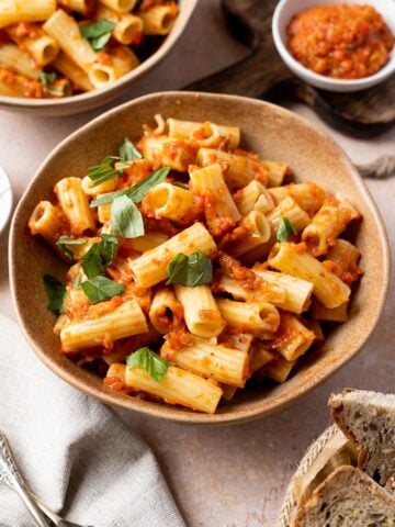 Ajvar pasta served with fresh chopped basil on top, bread and more sauce in a ramekin.