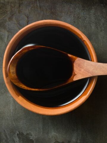 Dark soy sauce in a wooden bowl with a wooden spoon.