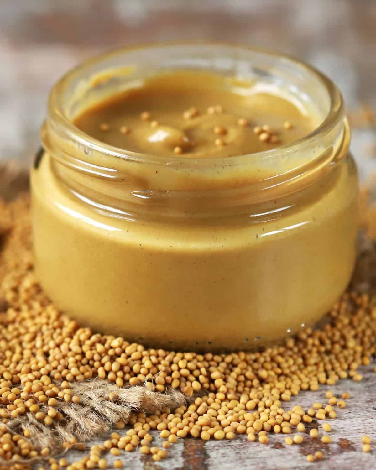 Mustard in a glass jar with mustard seeds surrounding it.