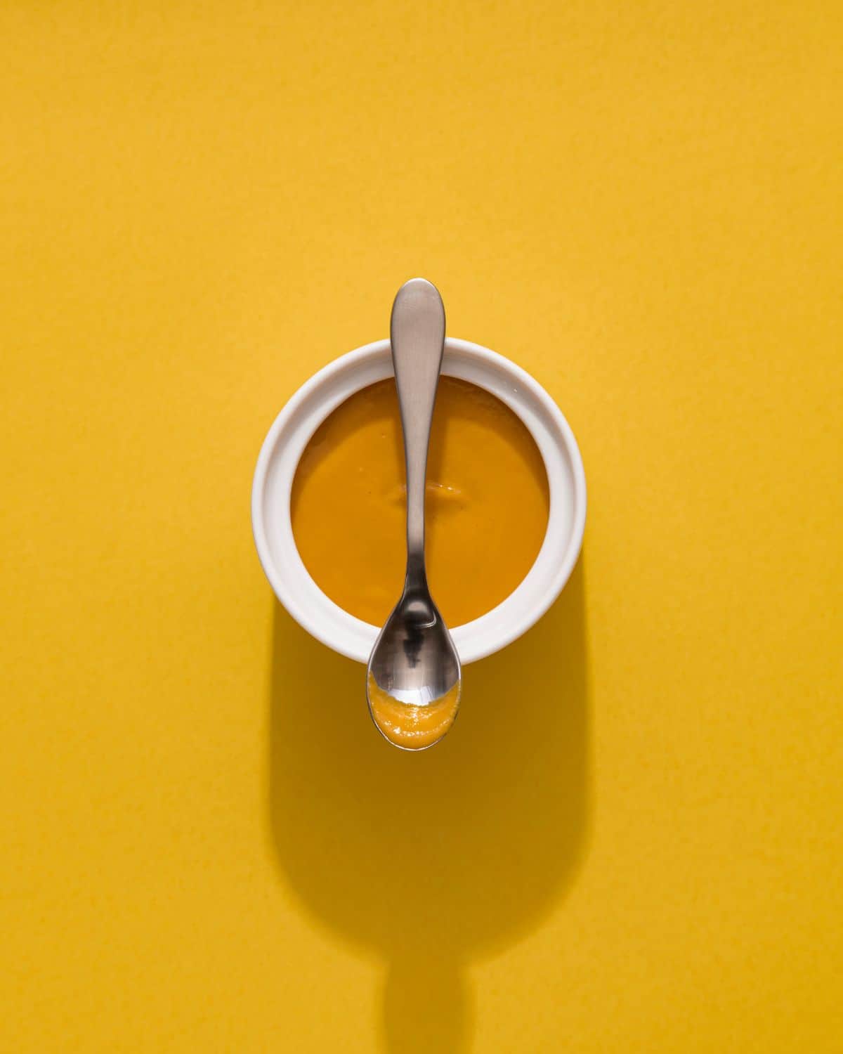 English mustard in a white ramekin with a teaspoon on top of it.
