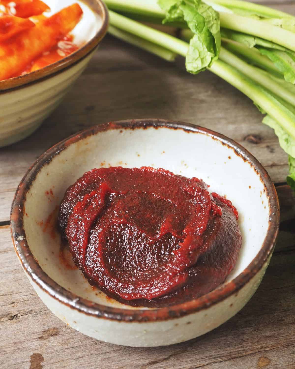 Gochujang paste in a bowl with salad items nearby.