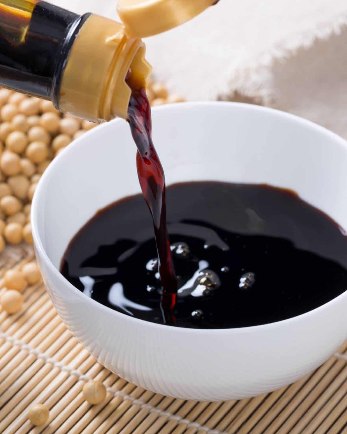 Soy sauce being poured into a bowl with soy beans in the background.