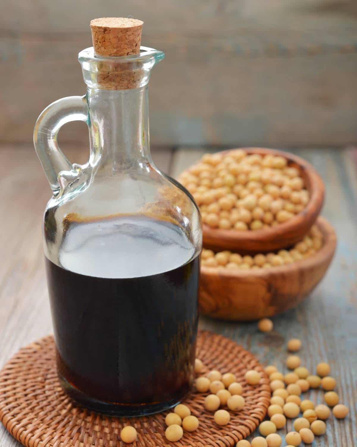 Soy sauce in a glass bottle with a handle and cork, soy beans in the background.