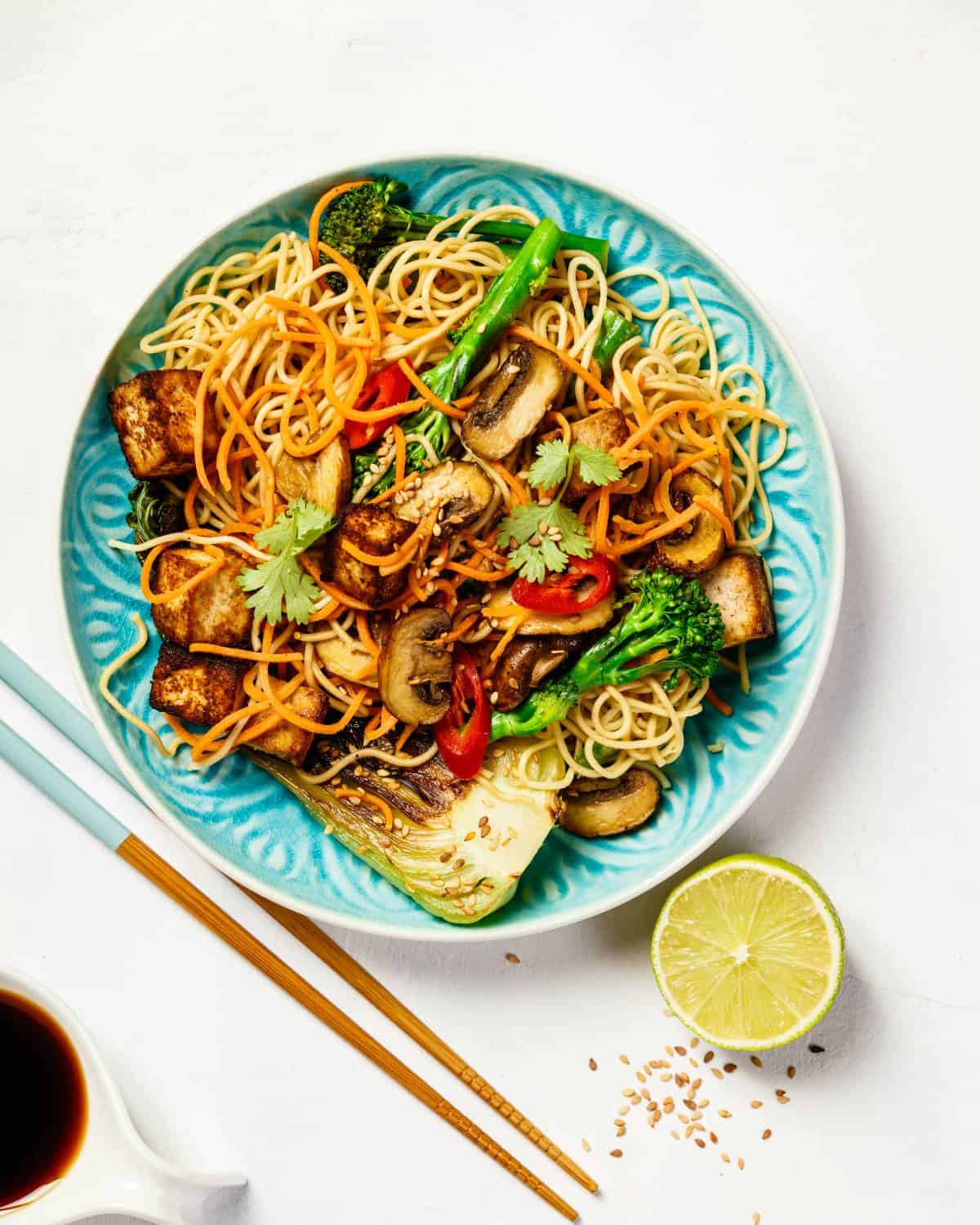 Vegetable stir fry with noodles, a soy sauce dipping bowl and chopsticks.