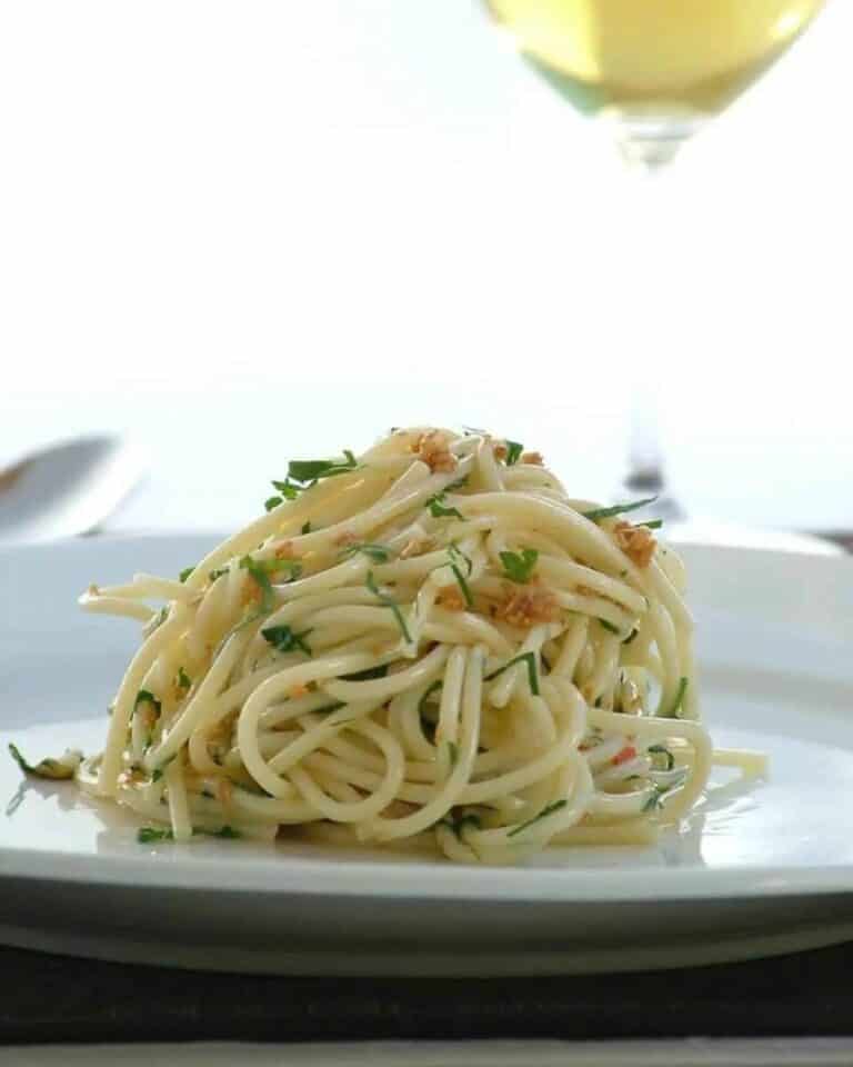 Spaghetti aglio e olio on a plate with a glass of white wine next to it.