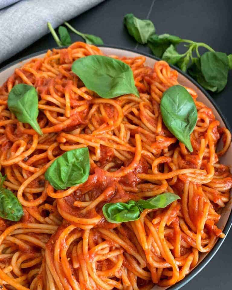 Spaghetti in tomato sauce with fresh basil leaves on top.