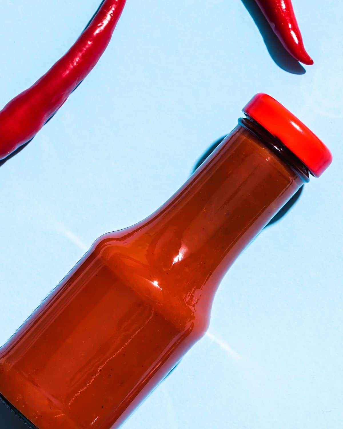 A bottle of ketchup with chilies near it.