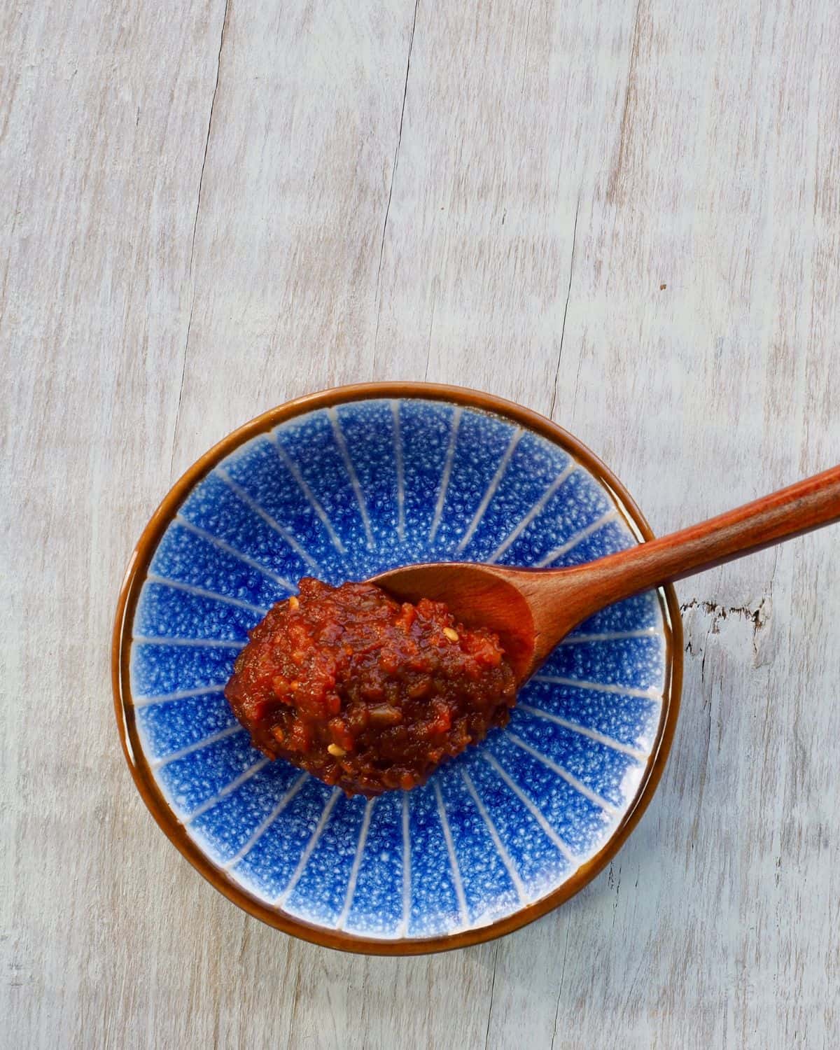 A bowl with a wooden spoon in it filled with ssamjang paste.