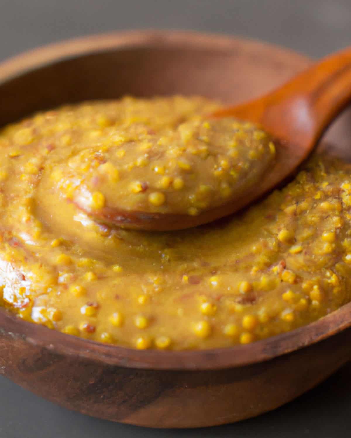 Sone ground mustard in a wooden bowl with a spoon.