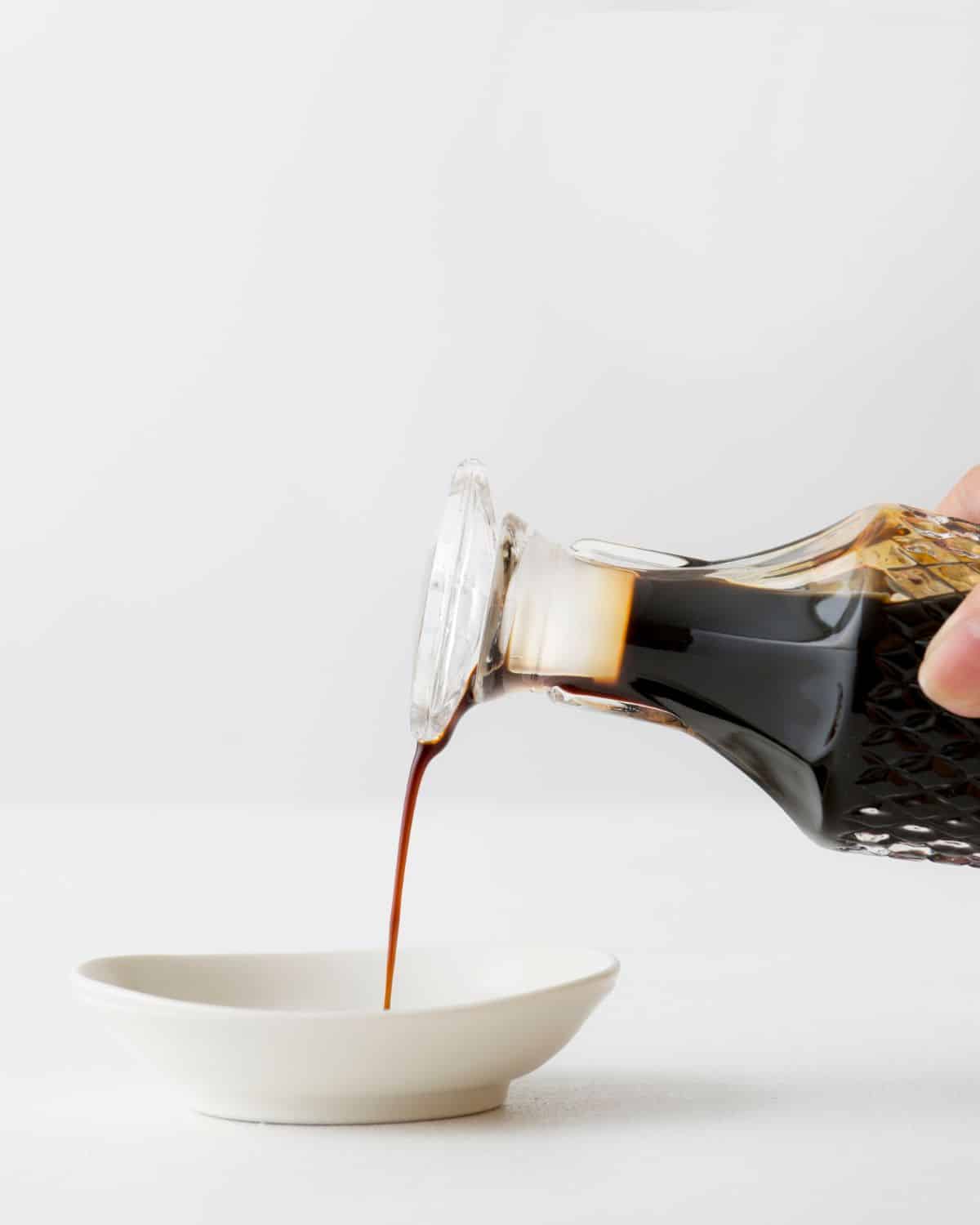 Glass bottle of tamari being poured into a small dish.