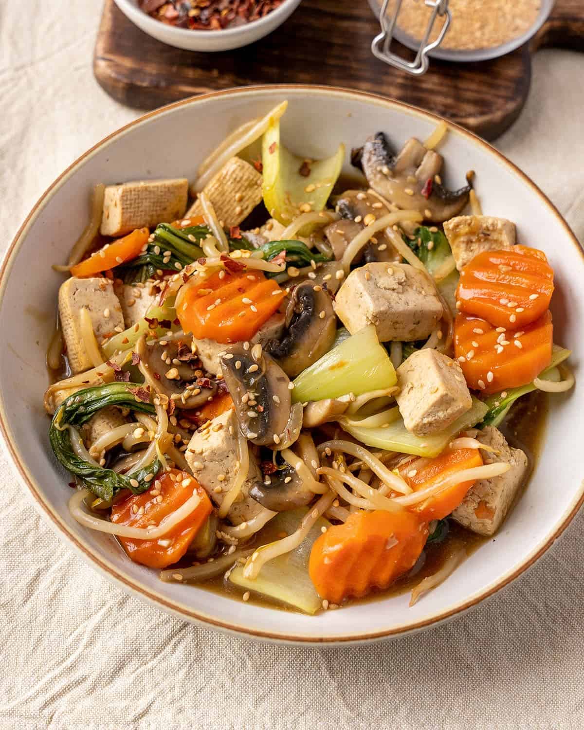 Carrots, mushrooms, bean sprouts and bok choy in a stir fry with tofu in a bowl.