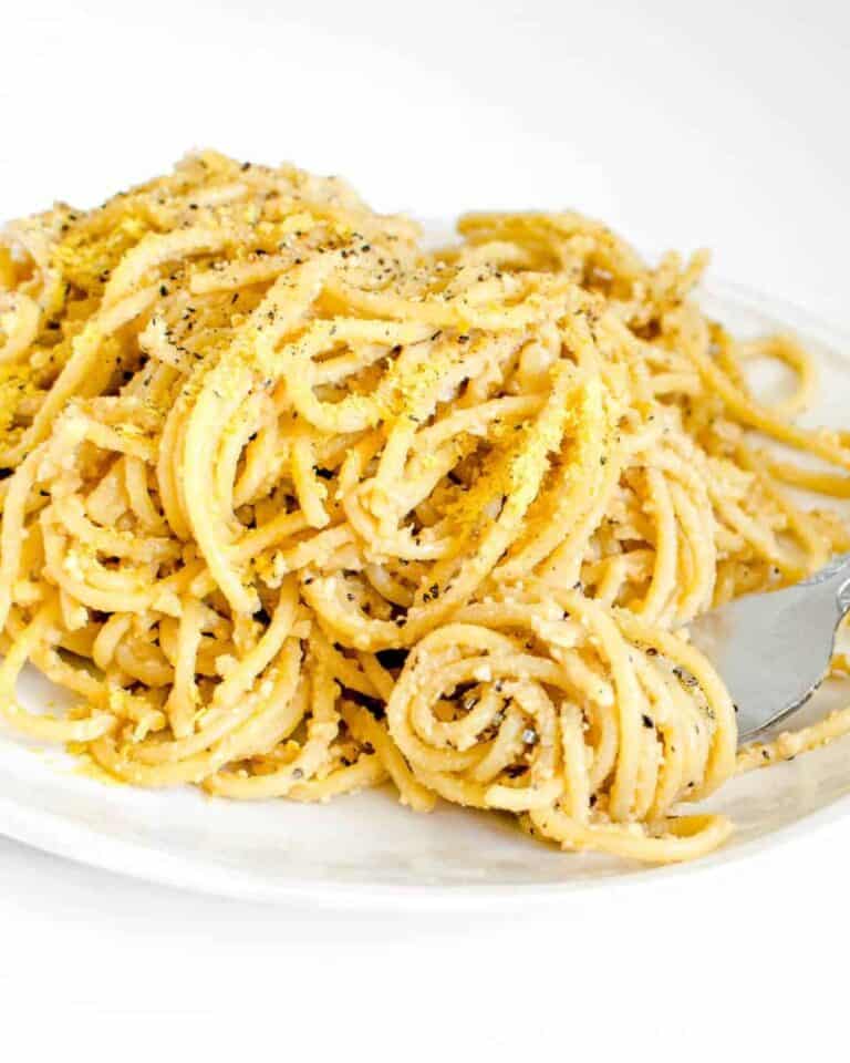 Vegan cacio e pepe on a plate with cracked black pepper and a fork.
