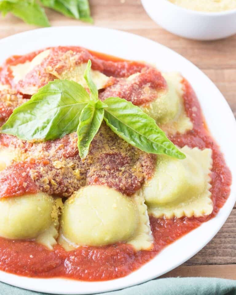 Vegan ravioli on a plate with marinara sauce topped with fresh basil.