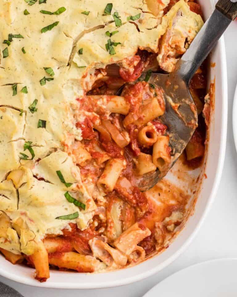 Vegan baked ziti in a casserole dish, topped with vegan creamy cheese sauce.