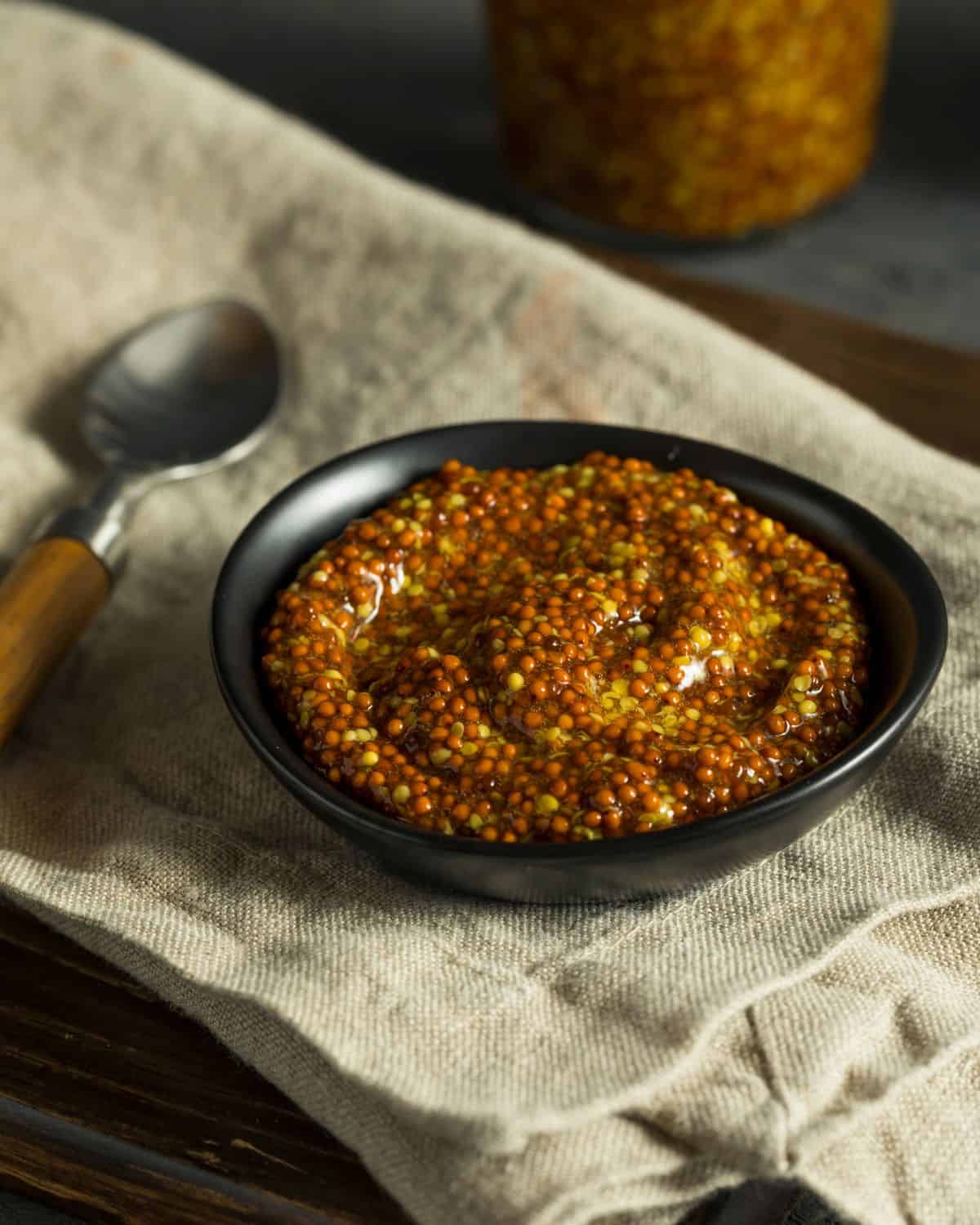 Wholegrain mustard in a bowl with a spoon next to it.