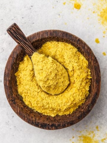 Nutritional yeast in a wooden bowl with a spoon.