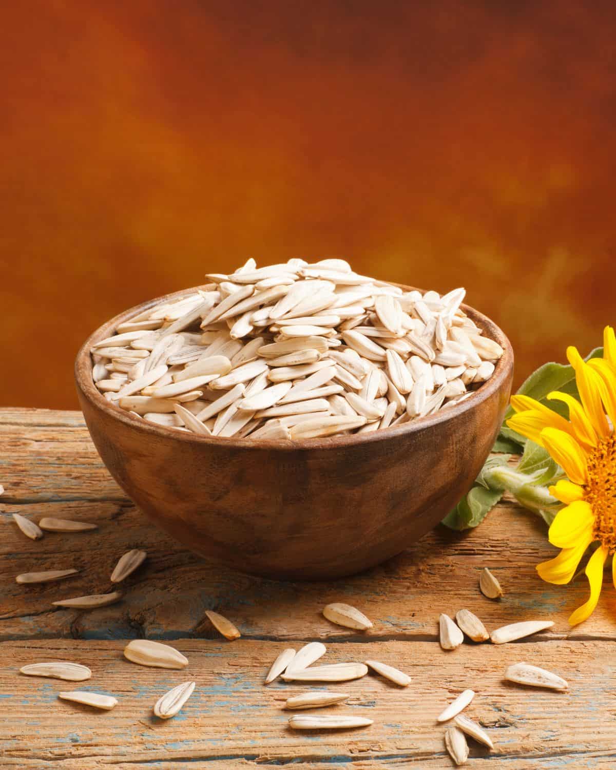 Sunflower seeds in a wooden bowl with a sunflower on a table.